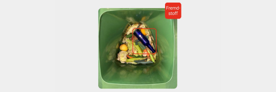Biotonne von oben mit erkannter Glasflasche als Fremdstoff im Müll.
