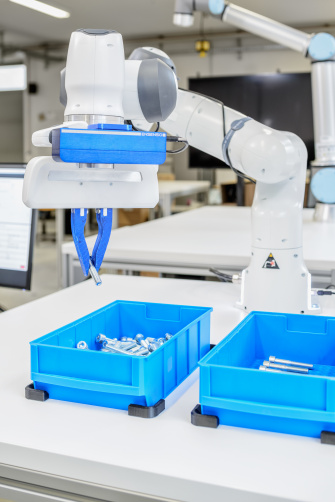 Ein Roboterarm mit Ensenso Kameras greift eine Schrauben aus blauen Behältnis.
