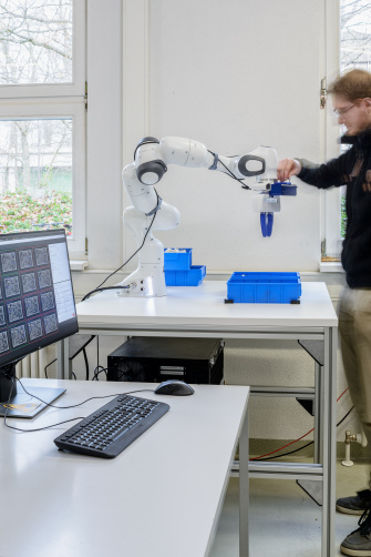 Ein Mann steht rechts neben einem Roboterarm und greift nach der befestigten Ensenso Kamera