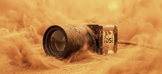 Industriekamera halb im Sand, umgeben von aufgewirbelten Sandwolken.