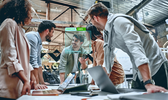 Zusammenarbeit: 5 Menschen stehen zusammen an Schreibtisch mit Laptops.