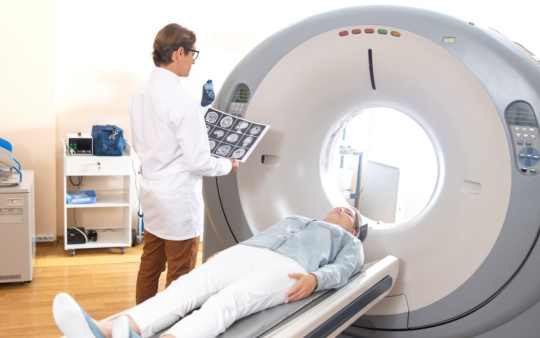 Arzt mit Hirnscans neben MRT-Gerät und liegendem Patienten.