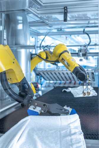 Zwei Roboter entfalten Wäsche in einer Großwäscherei mit Hilfe von IDS 2D- und 3D-Kameras.