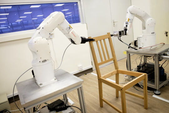 Zwei Roboterarme montieren einen Stuhl, der linke hält, der rechte schraubt