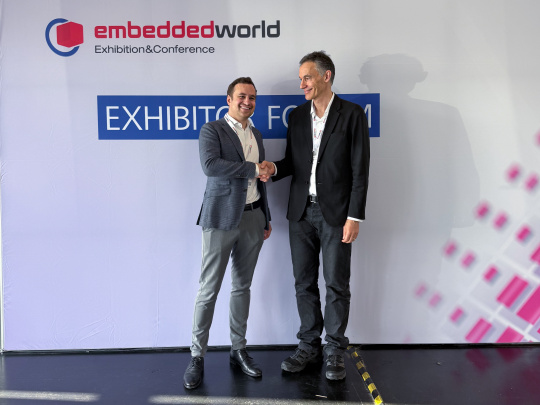 2 Geschäftsführer schütteln sich die Hand vor einer Messewand der Embedded World