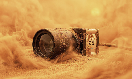 Industriekamera halb im Sand, umgeben von aufgewirbelten Sandwolken.
