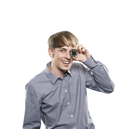 Ein Mann steht lachend vor weißem Hintergrund und verdeckt mit einer Platinenkamera eins seiner Augen.