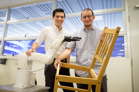 Zwei Wissenschaftler der Nanyang Technological University mit Stuhl und vor einem Roboter