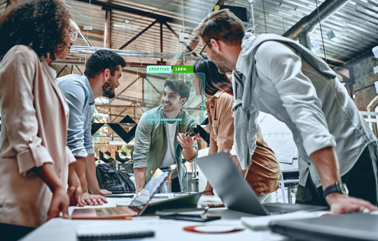Zusammenarbeit: 5 Menschen stehen zusammen an Schreibtisch mit Laptops.