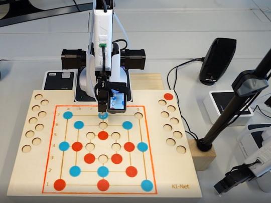 Roboterarm mit Kamera vor Mühle Spielbrett