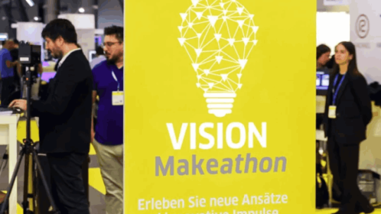 Gelber Messebanner „VISION Makeathon“ mit Glühbirnen-Grafik