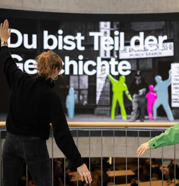 Zwei Personen posieren vor einer großen interaktiven Displaywand mit farbigen Silhouetten