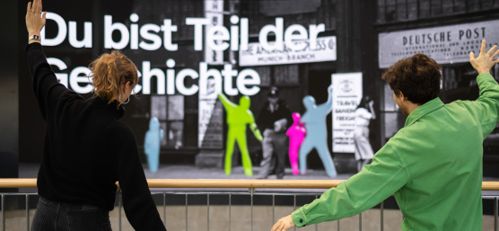 Zwei Personen posieren vor einer großen interaktiven Displaywand mit farbigen Silhouetten