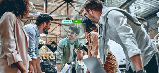 Zusammenarbeit: 5 Menschen stehen zusammen an Schreibtisch mit Laptops.