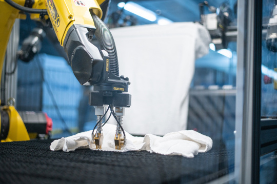 Ein gelber Roboter beim Entfalten eines Handtuchs in einer Großwäscherei.